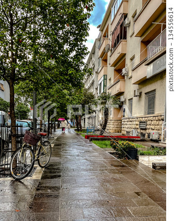 Cyclist resting by ornate railing on wet cobblestone street 134556614