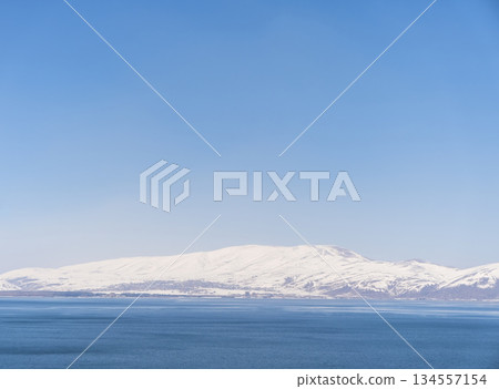 Aerial panorama view snow covered mountains. Snowy mountain ridge on winter sunrise. Stunning mountains range covered with snow over beautiful lake 134557154