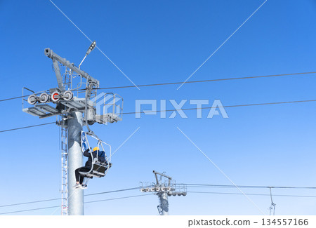 Ski chair lift over blue sky. Ski lift empty ropeway on hilghland mountain winter. Ski chairlift cable way with people enjoy skiing and snowboarding Ski chair lift over blue sky. Ski lift empty ropeway on hilghland mountain winter. Ski chairlift cable way with people enjoy skiing and snowboarding 134557166