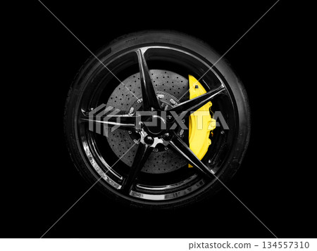 Car alloy wheel and tyre isolated on black background. New alloy wheel with tire and yellow carbon ceramic brakes. Alloy rim isolated. Car wheel disc. Car spare parts. 134557310