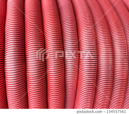 HDPE corrugated pipe texture background. Protection underground cable. Rolled up red corrugated PVC pipe. Red building pipes. Coated corrugated construction pipe. 134557561