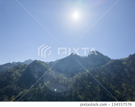 Scenic aerial mountain view to green forest valley in sunlight among mountain ranges and hills on horizon. Green landscape with sunlight mountains. 134557576