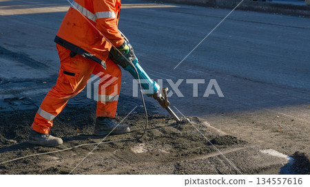 Men at work. Road worker breaks up old asphalt with a jackhammer 134557616