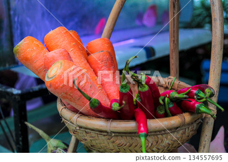 Close-up macro shot of vibrant red chili peppers and fresh organic carrots displayed together in a rustic woven bamboo basket with colorful bokeh background. Close-up macro shot of vibrant red chili peppers and fresh organic carrots displayed together in a rustic woven bamboo basket with colorful bokeh background. 134557695