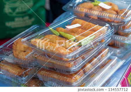 Close-up view of Gorengan (Indonesian Fried Snacks) packaged in clear rectangular plastic disposable boxes with raw green chilies displayed for purchase. Close-up view of Gorengan (Indonesian Fried Snacks) packaged in clear rectangular plastic disposable boxes with raw green chilies displayed for purchase. 134557712