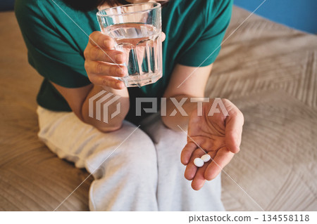Woman taking medication, holding medicine pills and glass of water 134558118
