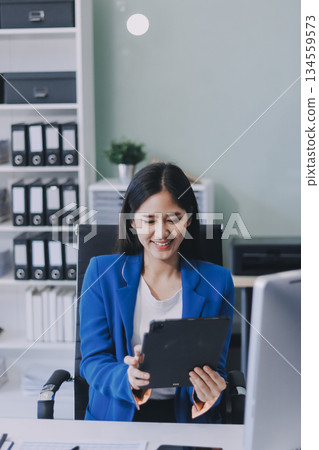 A smiling woman in a lab coat uses a tablet in a bright, modern environment. A smiling woman in a lab coat uses a tablet in a bright, modern environment. 134559573