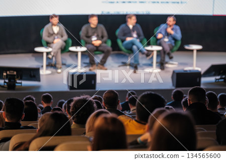 Panel discussion on stage with four speakers engaging audience in conference setting Panel discussion on stage with four speakers engaging audience in conference setting 134565600