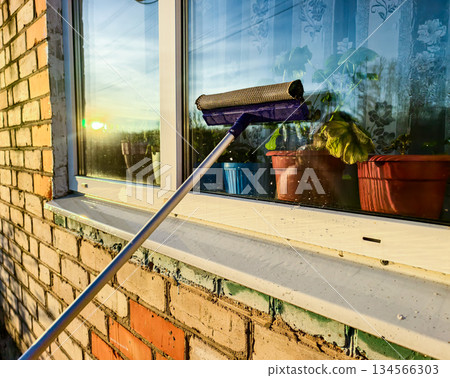 Window cleaning. Window cleaning tools. Applying soapy water to the window glass, reflecting sunlight and houseplants through the glass, and demonstrating household cleaning techniques. Window cleaning. Window cleaning tools. Applying soapy water to the window glass, reflecting sunlight and houseplants through the glass, and demonstrating household cleaning techniques. 134566303
