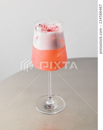 Chic coral cocktail featuring frothy finish and petal garnish 134566467
