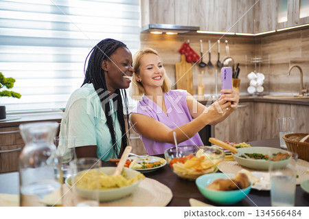 Two friends capturing joyful moments during a cozy dinner 134566484
