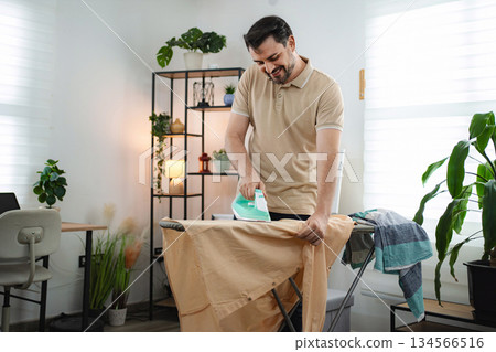 Man smiling while ironing clothes at home 134566516