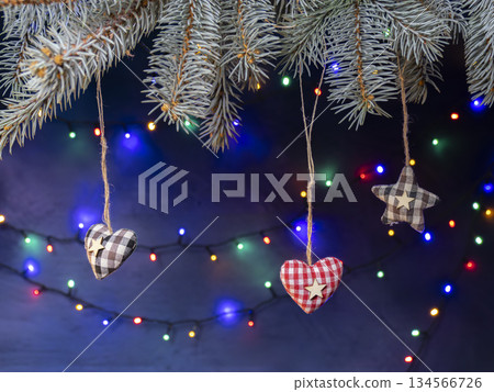 Hanging Fabric Hearts And Stars On Christmas Tree Branches With Colorful Holiday Lights Hanging Fabric Hearts And Stars On Christmas Tree Branches With Colorful Holiday Lights 134566726