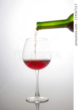 a green wine bottle filling a crystal wine glass with deep red wine, showcasing bubbles and flow a green wine bottle filling a crystal wine glass with deep red wine, showcasing bubbles and flow 134567317