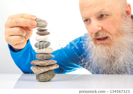 Enthusiastic older man smiling widely while engaged in building a stack of assorted stone Enthusiastic older man smiling widely while engaged in building a stack of assorted stone 134567323