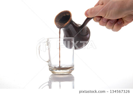 Rich coffee flows from a vintage ceramic pot into a clear glass cup 134567326