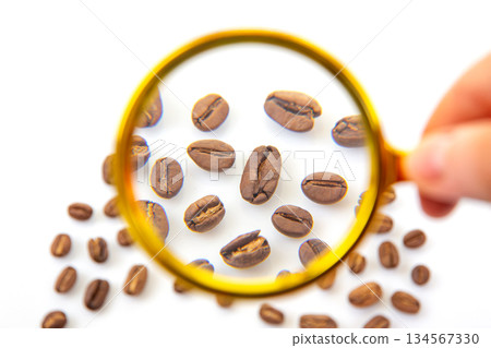 Magnifying glass and coffee beans arranged on a plain white background 134567330