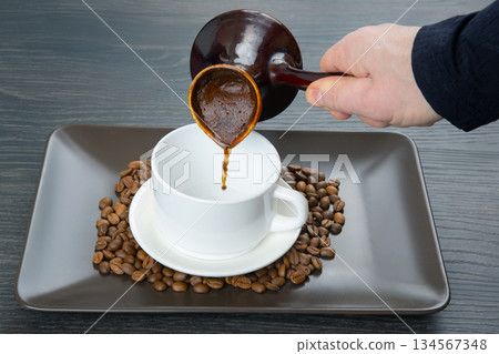A hand skillfully pours aromatic Turkish coffee from a classic cezve into a white cup 134567348