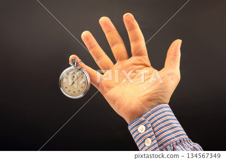hand with a mechanical analog stopwatch on a dark background. hand with a mechanical analog stopwatch on a dark background. 134567349