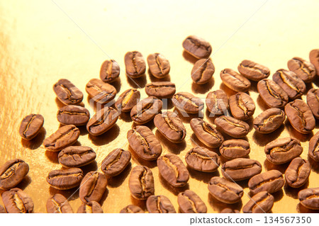 A collection of roasted coffee beans shaped into an oval on a shiny gold background A collection of roasted coffee beans shaped into an oval on a shiny gold background 134567350