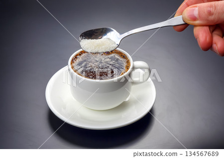 Pouring sugar into hot coffee in a white cup on a dark background 134567689