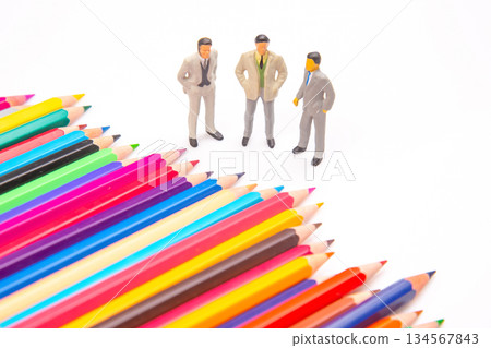 colored pencils fanned out on a white backdrop, paired with three miniature business figures 134567843