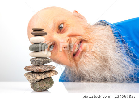 Enthusiastic older man smiling widely while engaged in building a stack of assorted stones Enthusiastic older man smiling widely while engaged in building a stack of assorted stones 134567853