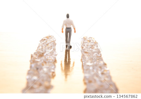 A small businessman walks between gleaming crystal piles on a reflective golden floor A small businessman walks between gleaming crystal piles on a reflective golden floor 134567862