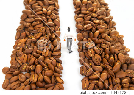 A symbolic stock photo of a miniature figure in a suit walking between piles of coffee beans A symbolic stock photo of a miniature figure in a suit walking between piles of coffee beans 134567863