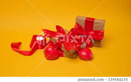 Gifts wrapped in brown paper and red satin ribbon on a yellow background, holiday Gifts wrapped in brown paper and red satin ribbon on a yellow background, holiday 134568235
