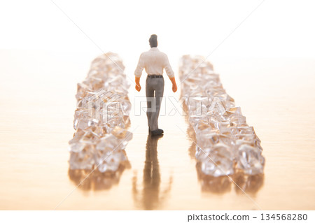 A small businessman walks between gleaming crystal piles on a reflective golden floor A small businessman walks between gleaming crystal piles on a reflective golden floor 134568280