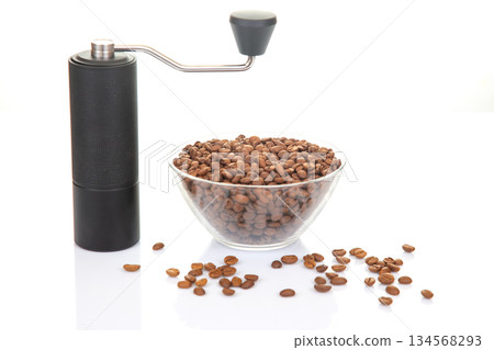 A stylish black manual coffee grinder paired with a glass bowl of freshly roasted coffee beans 134568293