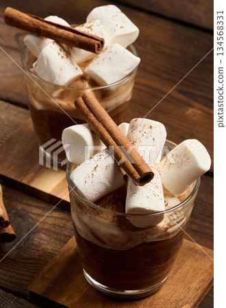 A glass of hot chocolate with fluffy marshmallows on a wooden table. A glass of hot chocolate with fluffy marshmallows on a wooden table. 134568331
