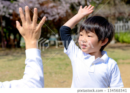 一位父親稱讚孩子做得好的地方，兩人擊掌，一對父母和孩子在公園裡玩接球遊戲 134568341