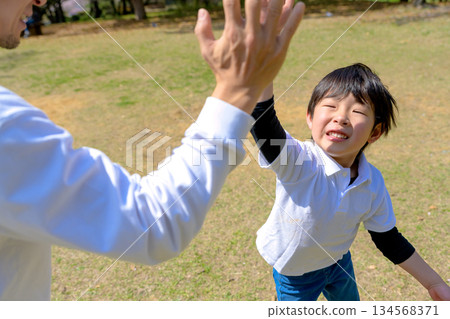 一位父親稱讚孩子做得好的地方,兩人擊掌,一對父母和孩子在公園裡玩接球遊戲 一位父親稱讚孩子做得好的地方,兩人擊掌,一對父母和孩子在公園裡玩接球遊戲 134568371