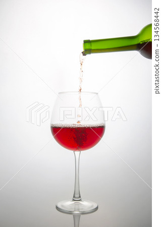 Dynamic shot of a green bottle pouring vibrant red wine into a delicate glass Dynamic shot of a green bottle pouring vibrant red wine into a delicate glass 134568442
