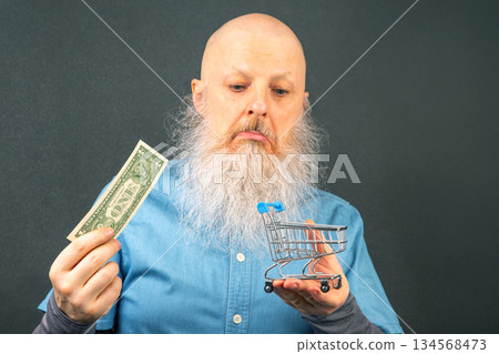 bald man with a large white beard holds a dollar and a model of a grocery basket bald man with a large white beard holds a dollar and a model of a grocery basket 134568473