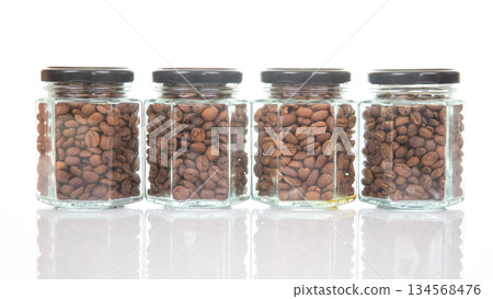 Four glass jars with black lids filled with roasted coffee beans Four glass jars with black lids filled with roasted coffee beans 134568476