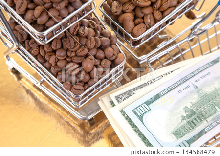On a golden surface, a cart of roasted coffee beans pairs with 100 bills On a golden surface, a cart of roasted coffee beans pairs with 100 bills 134568479