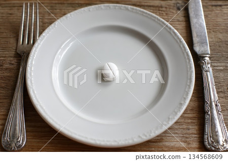 White pill resting on a plate with silver cutlery on a wooden table 134568609