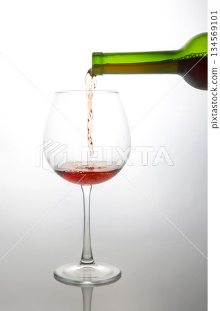 Dynamic shot of a green bottle pouring vibrant red wine into a delicate glass Dynamic shot of a green bottle pouring vibrant red wine into a delicate glass 134569101