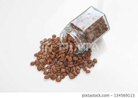 roasted coffee beans poured out of a glass transparent jar on a white background. roasted coffee beans poured out of a glass transparent jar on a white background. 134569113