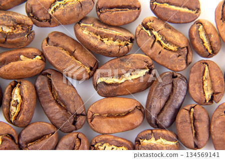 Detailed view of roasted coffee beans, displaying their cracked surfaces Detailed view of roasted coffee beans, displaying their cracked surfaces 134569141