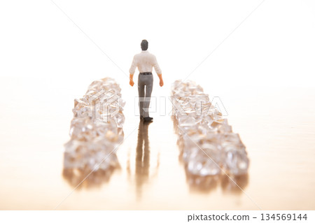 A small businessman walks between gleaming crystal piles on a reflective golden floor A small businessman walks between gleaming crystal piles on a reflective golden floor 134569144