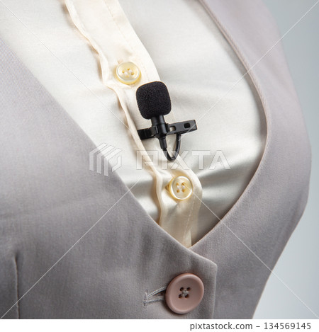 A black lavalier microphone with a clip is attached to a cream-colored button-up shirt 134569145