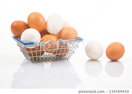 White and brown eggs in a wire shopping basket, accompanied by two eggs White and brown eggs in a wire shopping basket, accompanied by two eggs 134569450