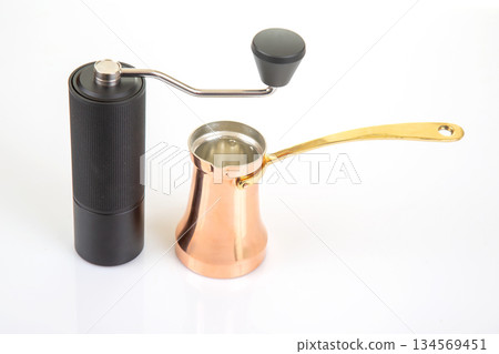 sleek black coffee grinder and a shiny copper cezve with a gold handle sleek black coffee grinder and a shiny copper cezve with a gold handle 134569451