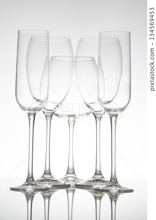 A row of five empty wine glasses with elegant stems, reflecting perfectly on a glossy table A row of five empty wine glasses with elegant stems, reflecting perfectly on a glossy table 134569453