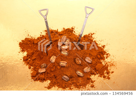 Two metal shovels stand in a mound of ground coffee with scattered coffee beans Two metal shovels stand in a mound of ground coffee with scattered coffee beans 134569456