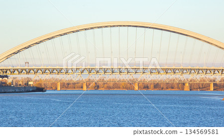 Clear evening view of a large arch bridge spanning a river with calm water reflections Clear evening view of a large arch bridge spanning a river with calm water reflections 134569581